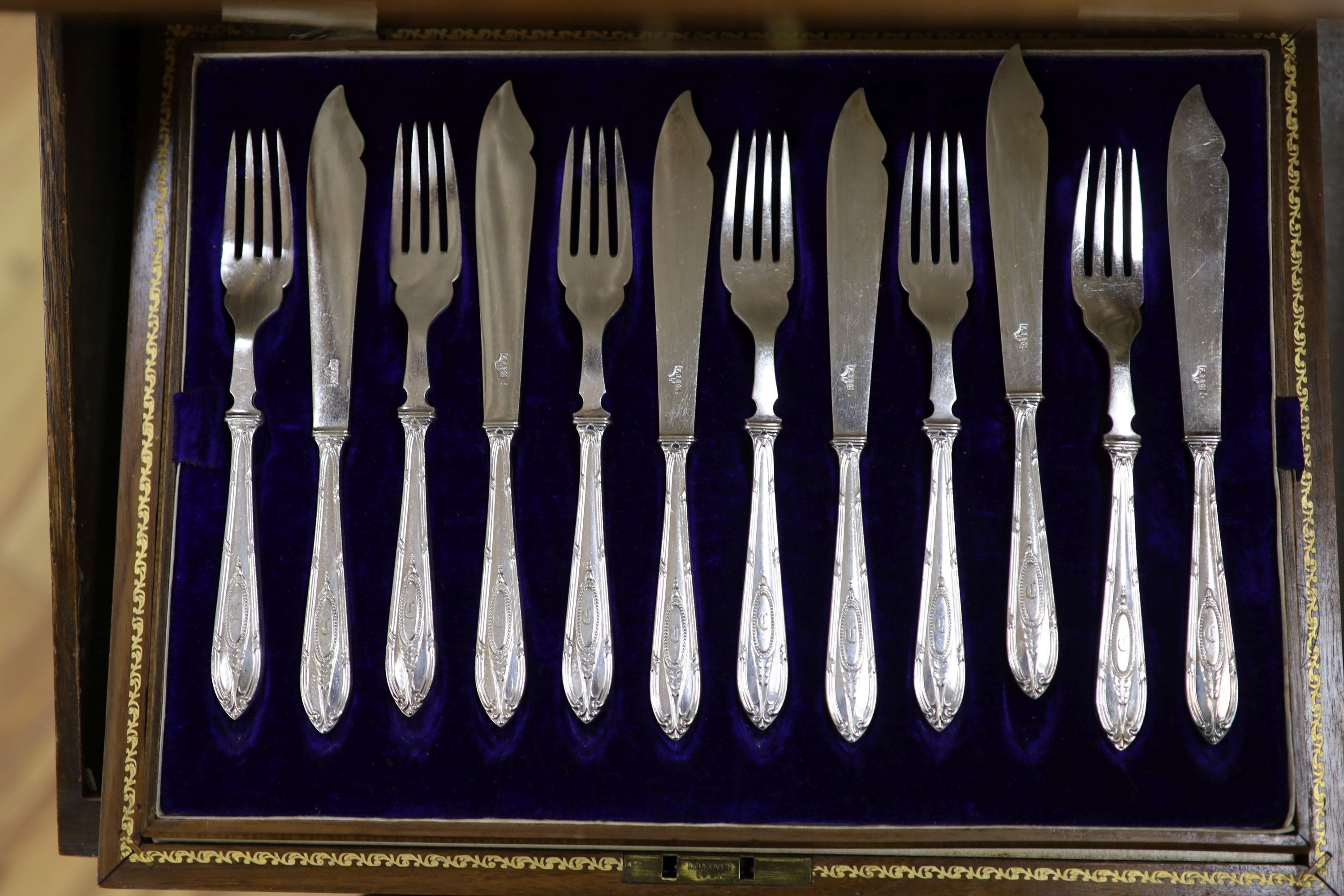 An Edwardian oak cased silver plated table canteen, settings for twelve and a set of silver plated fish knives and forks for twelve